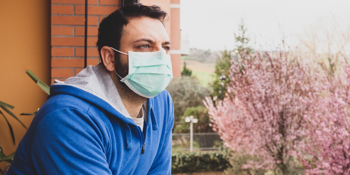 giovane guarda alla finestra con la mascherina protettiva